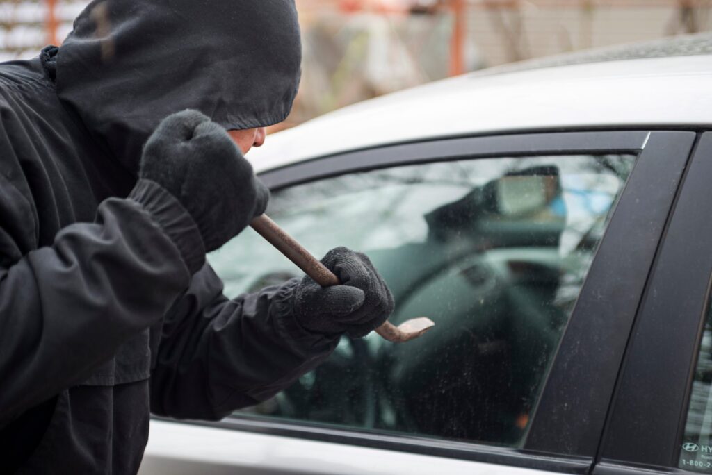 Lladre a punt de trencar el vidre d'un cotxe: robatori del vehicle